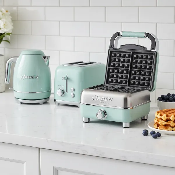 A retro-chic Haden Heritage waffle maker in pastel teal with chrome accents, sitting on a stylish kitchen counter.